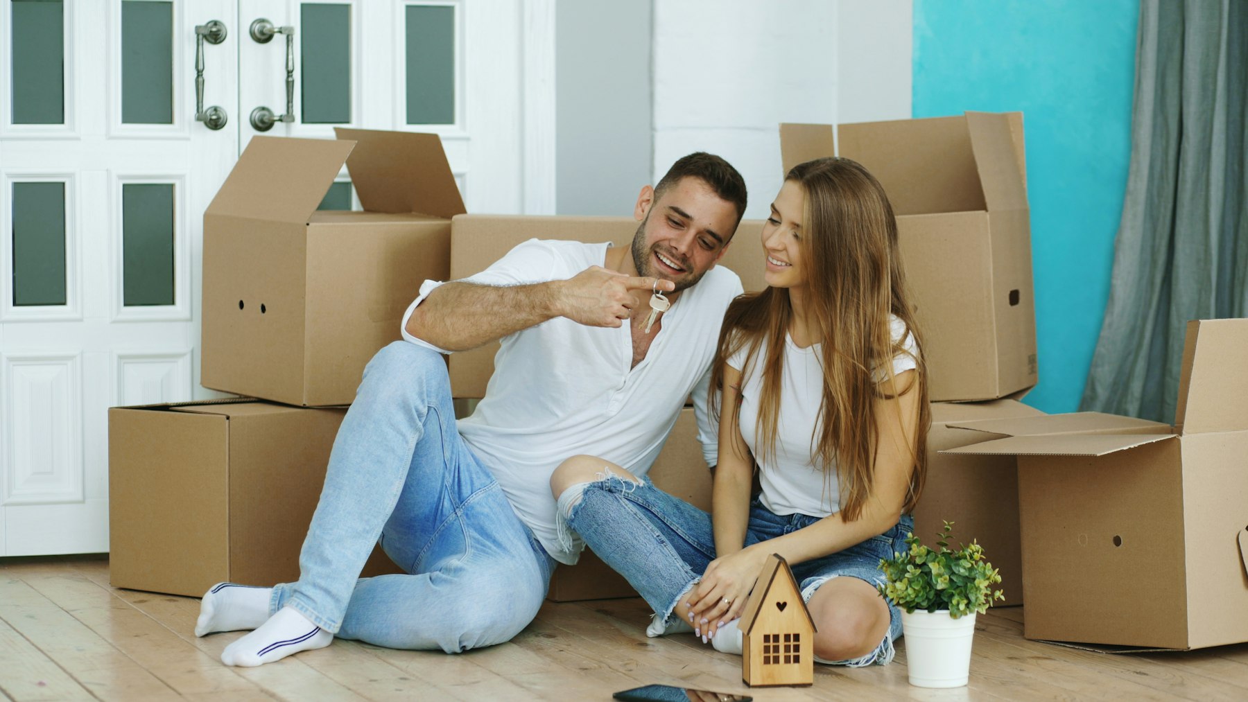 A couple sitting among moving boxes with the key to their new home