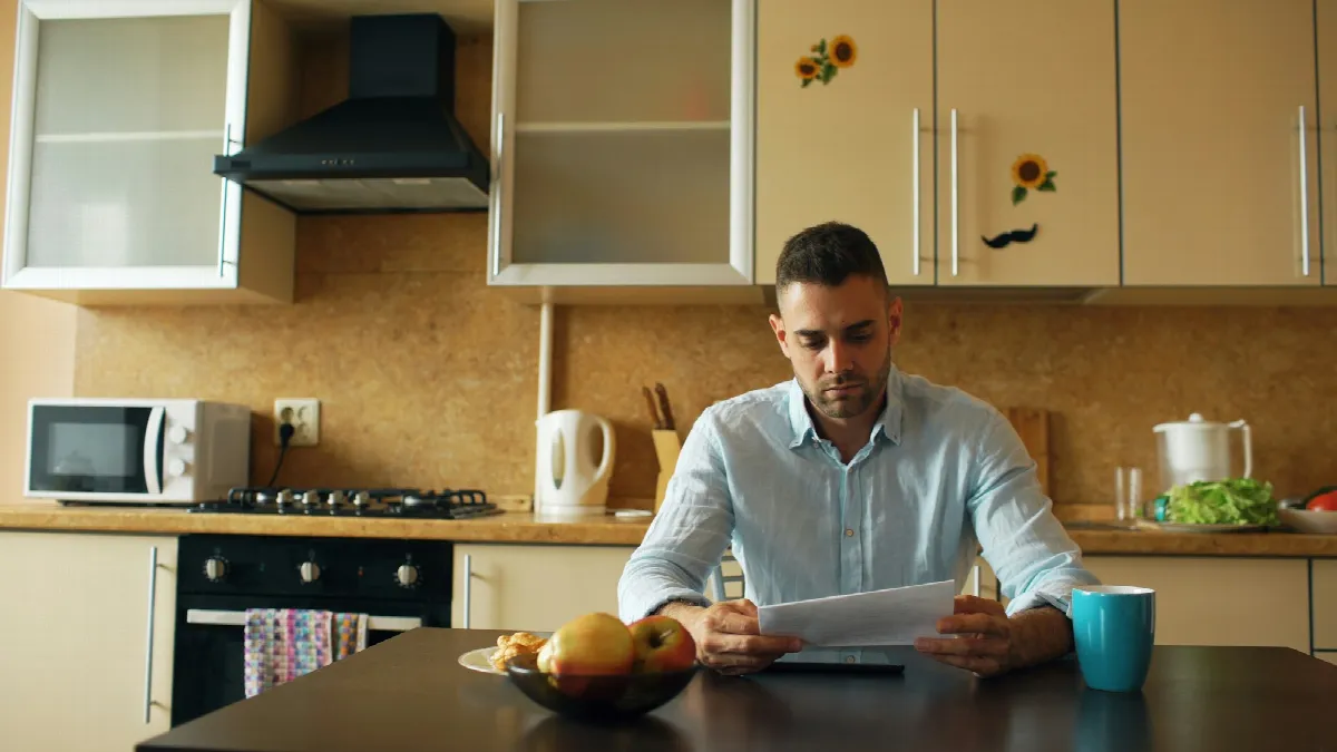 A man reads loan documents at his kitchen table over coffee, the kind of review to do before you cosign a loan
