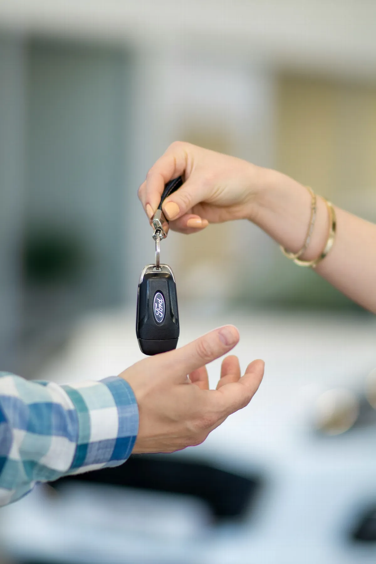 One person hands a car key on a fob to another person in front of a white car