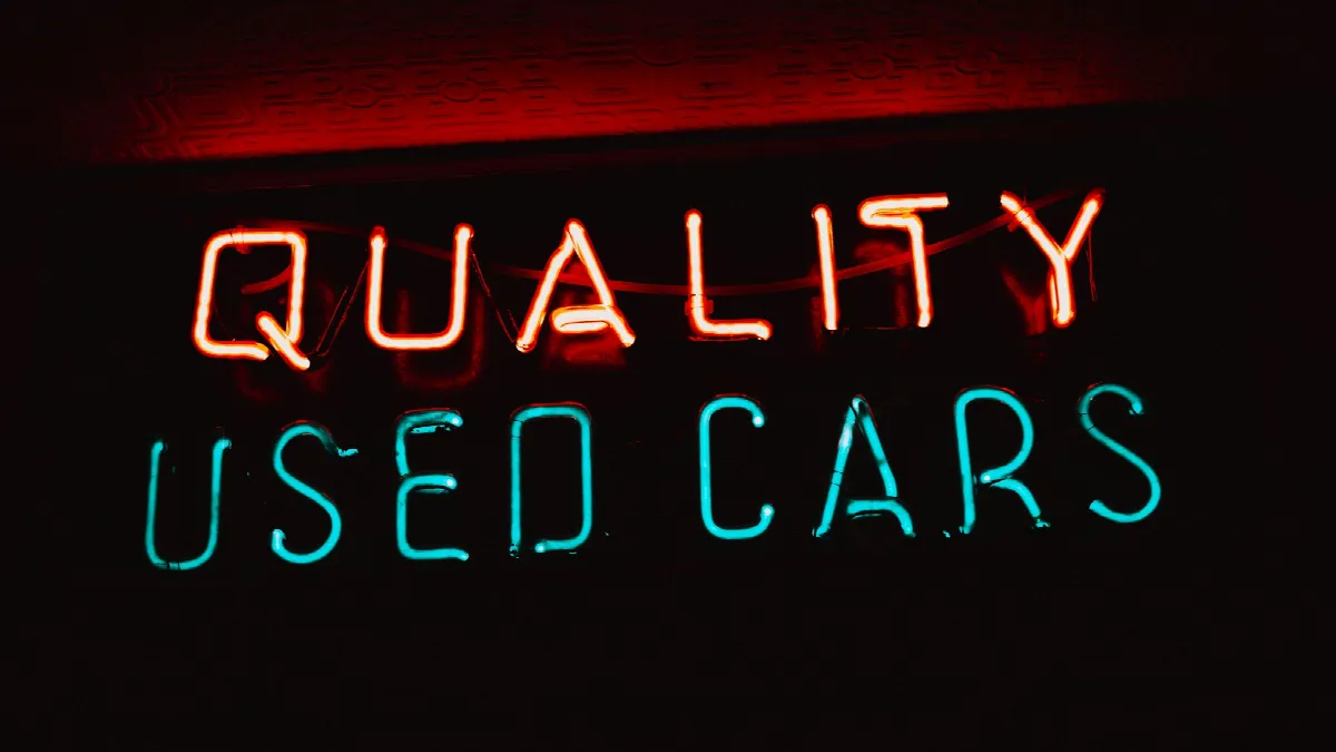 A neon sign in a dealership window that reads Quality Used Cars