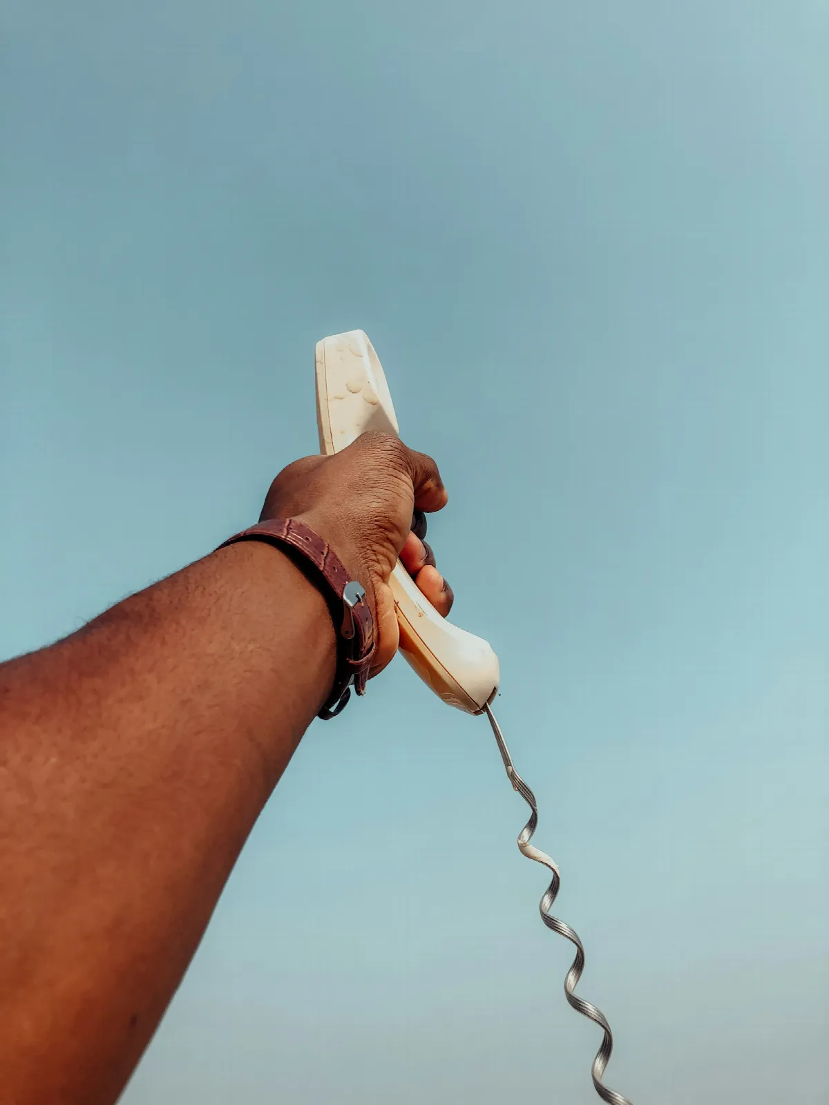 A hand holding a white corded desk phone, the kind of landline most likely to return a clean caller ID name lookup