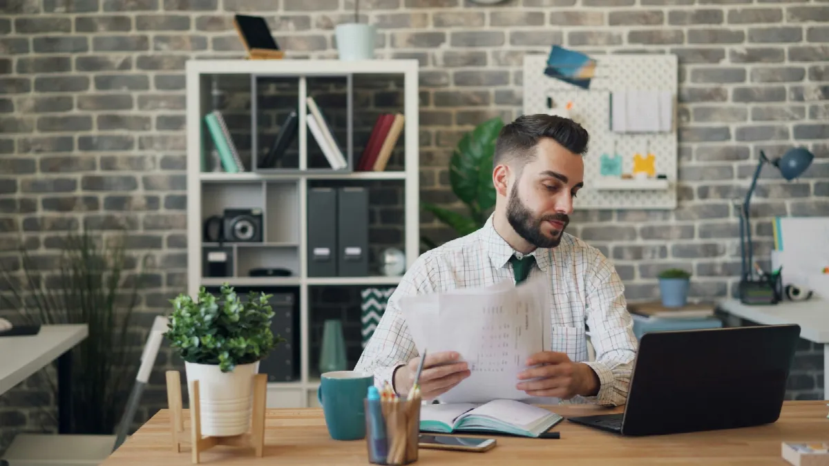 A man working at a desk with a laptop and printed papers spread in front of him