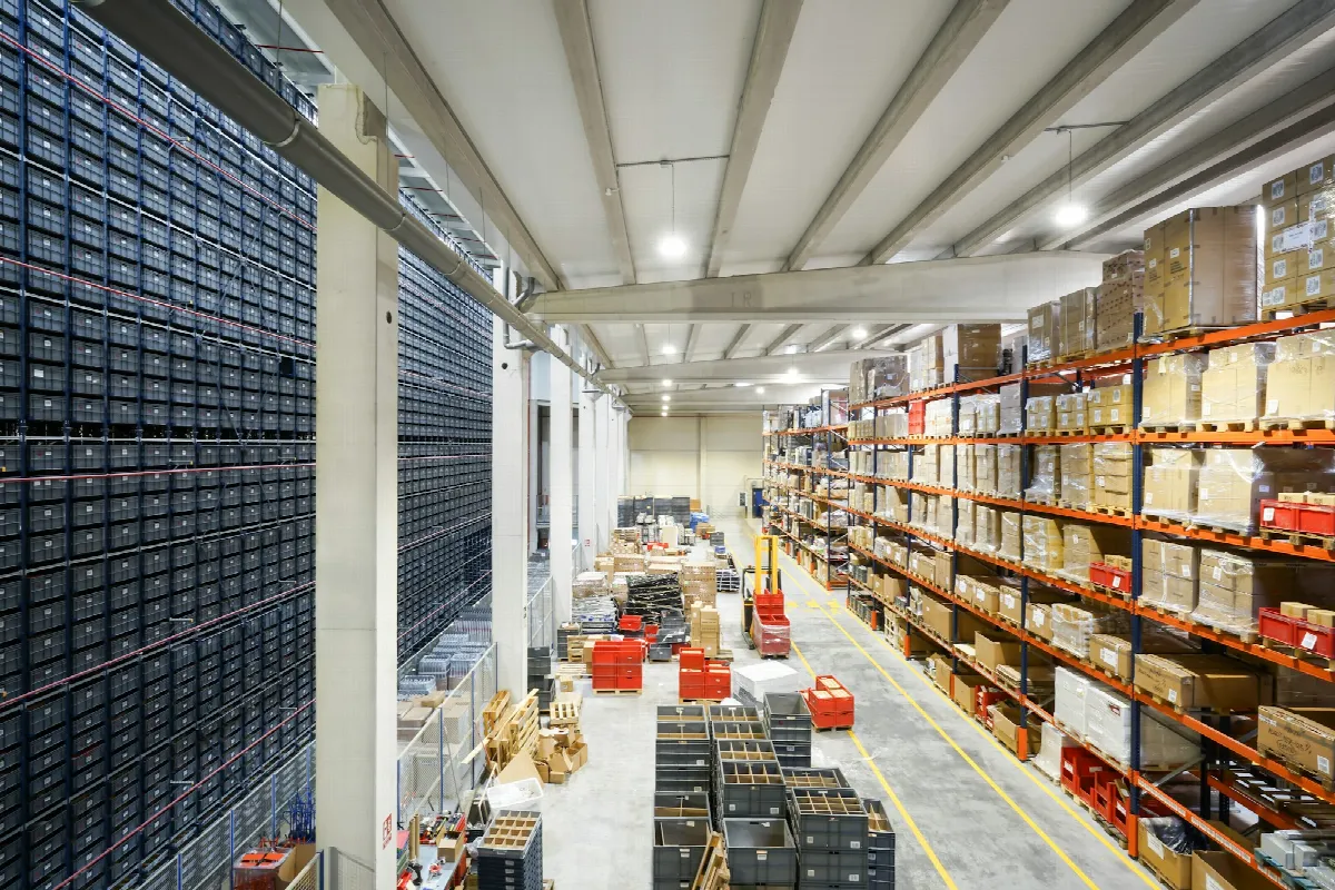 A long warehouse aisle lined with tall shelves of boxed inventory and crates on the floor