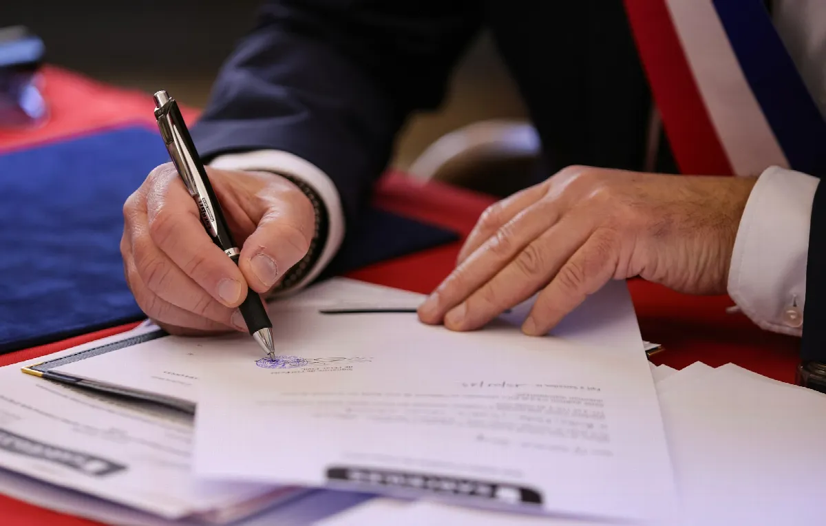 A person in a suit signing a printed document with a silver pen