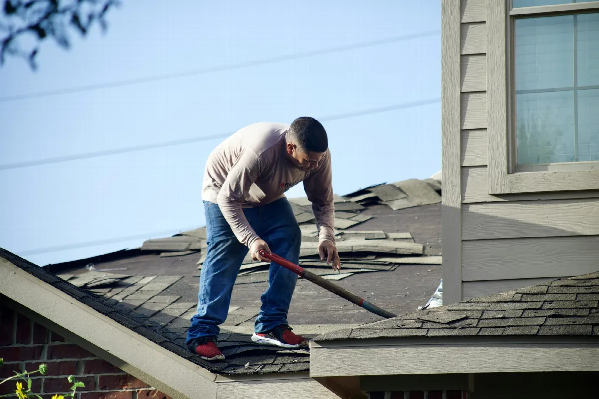 A roofer tears old shingles off a house on a clear day, the kind of big job where a contractor client credit check pays off
