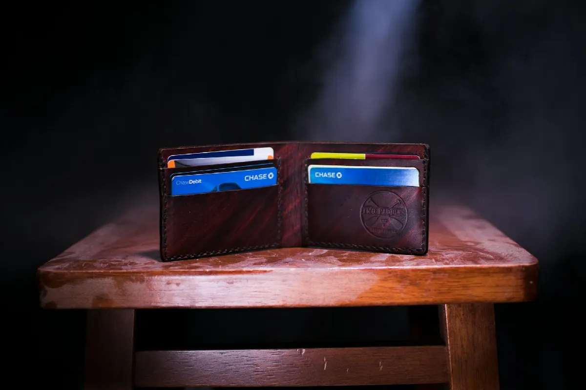 An open brown leather wallet holding several credit cards, standing on a small wooden table in a dark room