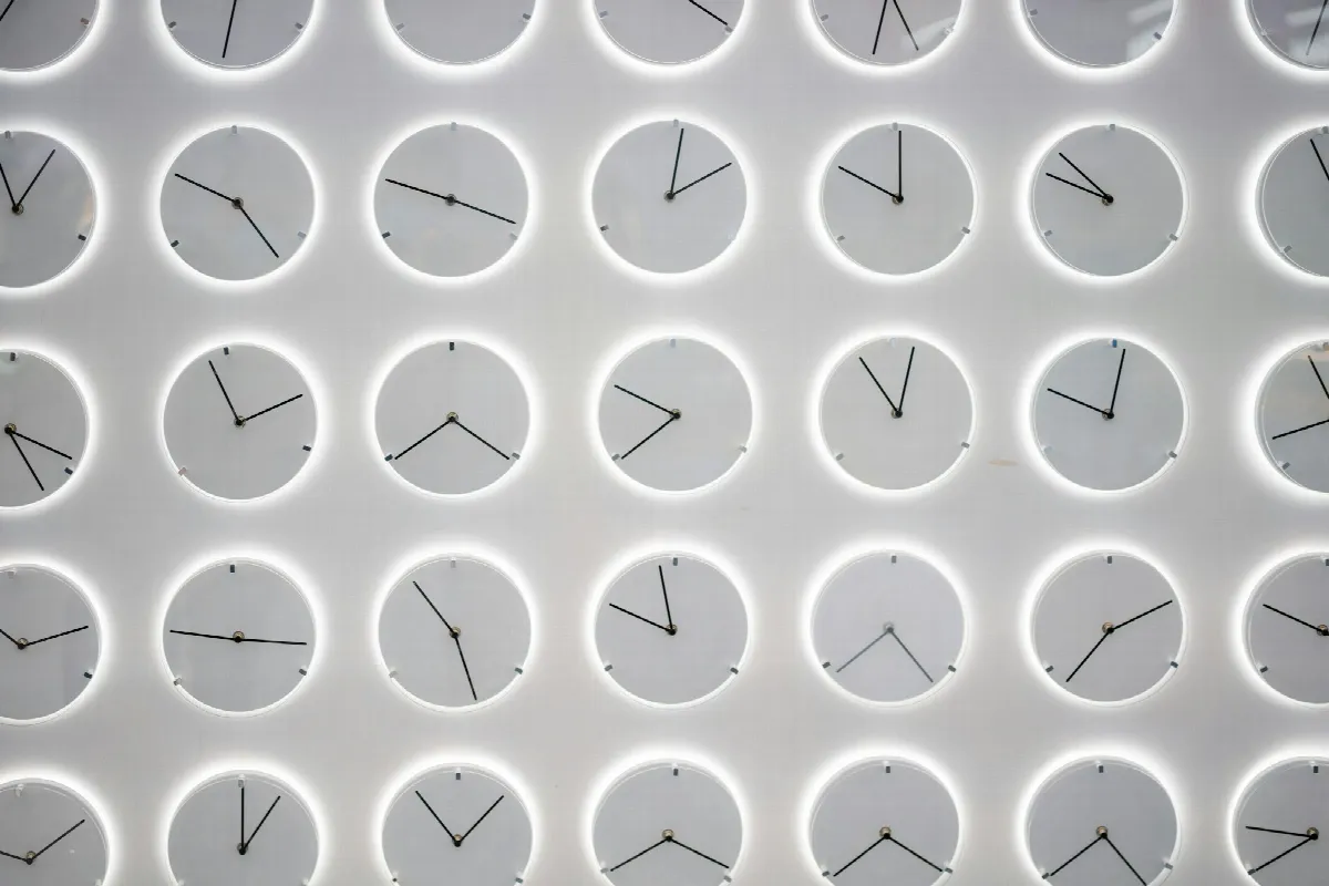 A white wall covered with rows of identical round clocks, each one showing a different time