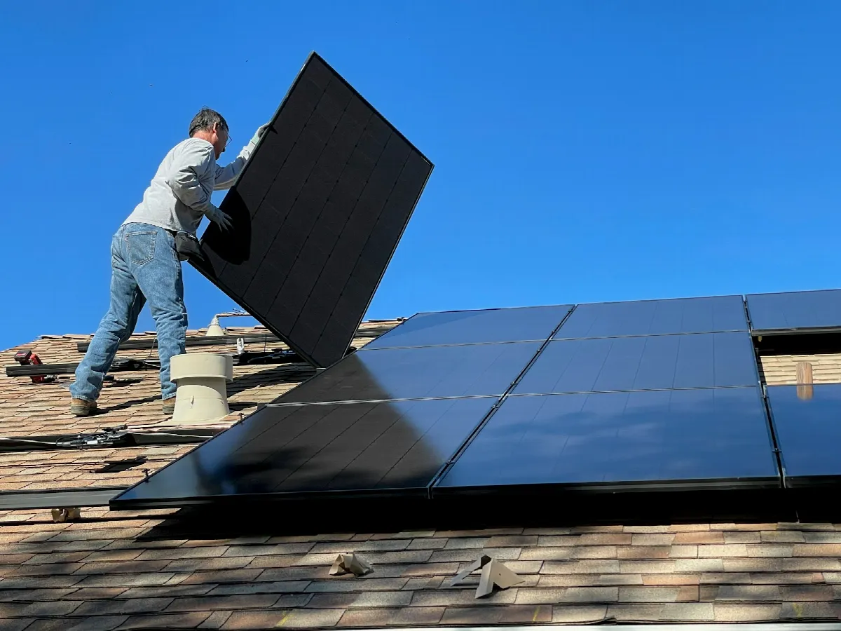 An installer lifts a black solar panel onto a shingled roof, a job that often starts with home improvement financing prequalification