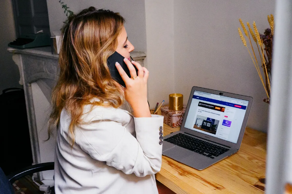 A woman working at a desk with a laptop open and a smartphone in her hand