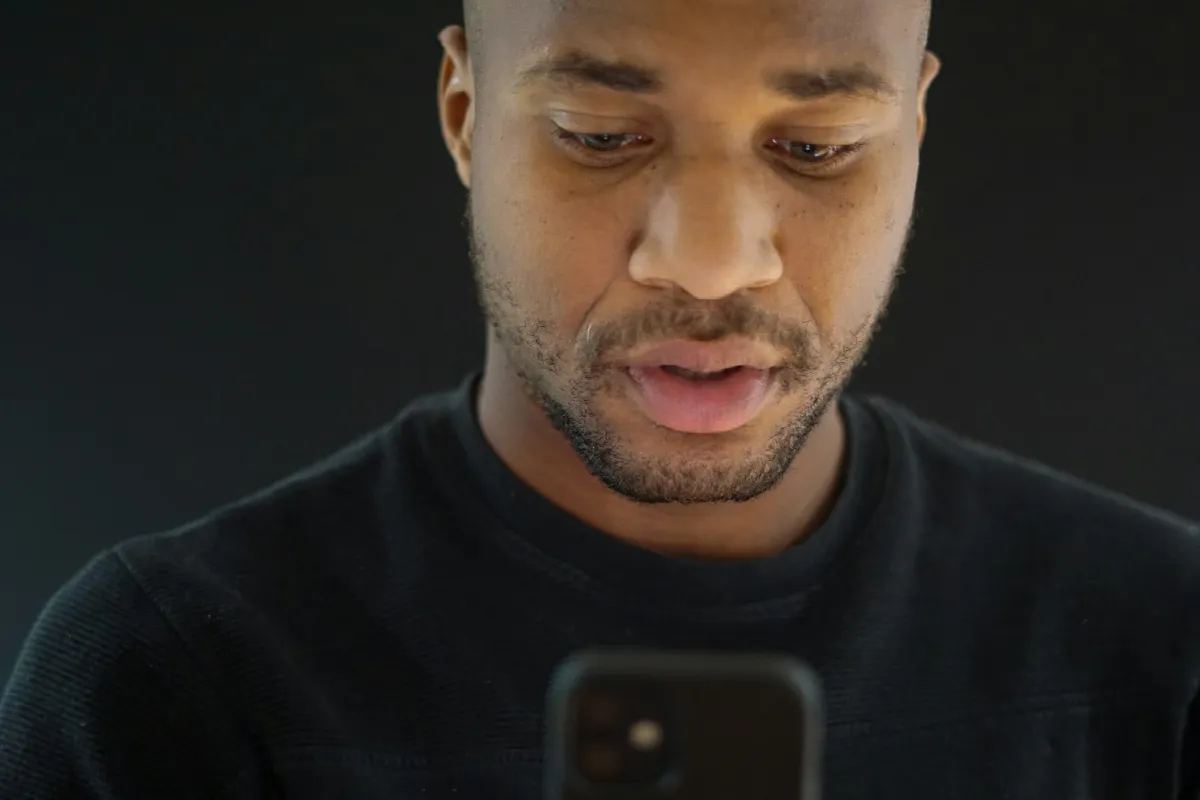 A man in a dark sweater looks down at his phone, trying to work out who owns this phone number