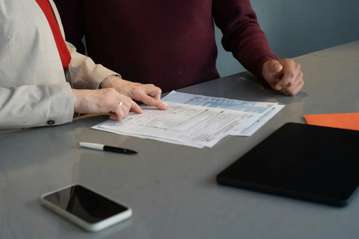 Two people at a gray table go over a signed consent form before they look up someone's credit score, with a pen and phone nearby