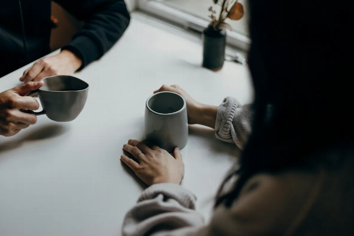 Two friends at a table holding gray coffee mugs, the kind of conversation that comes before lending money to a friend