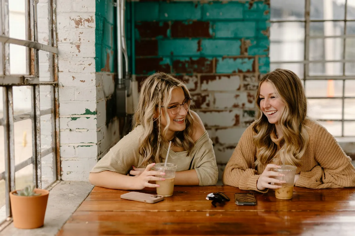 Two women sitting at a table with drinks, talking face to face