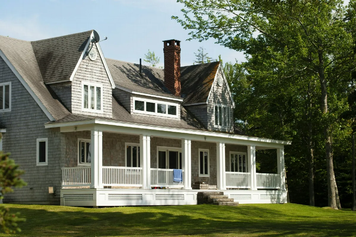 A white and brown wooden house with a front porch surrounded by green trees