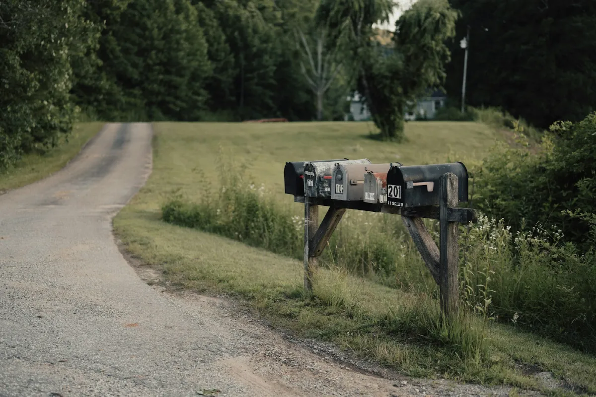 A row of rural mailboxes on a wooden post beside a gravel road, the kind that fill up with pre-approved mail until you opt out of prescreened offers