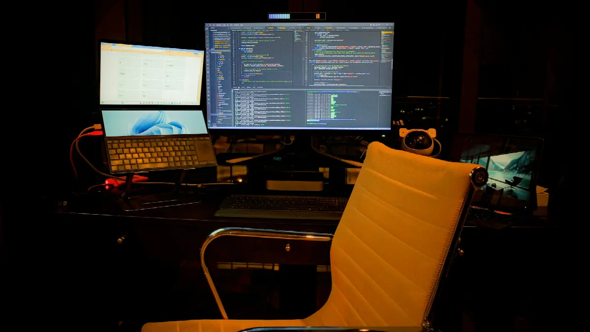 A dark home office with a laptop and a large monitor showing code, set up for a CRM credit check integration