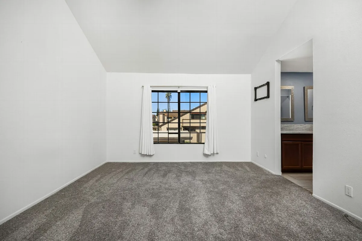 An empty carpeted bedroom with white walls and a single window, waiting for its next tenant