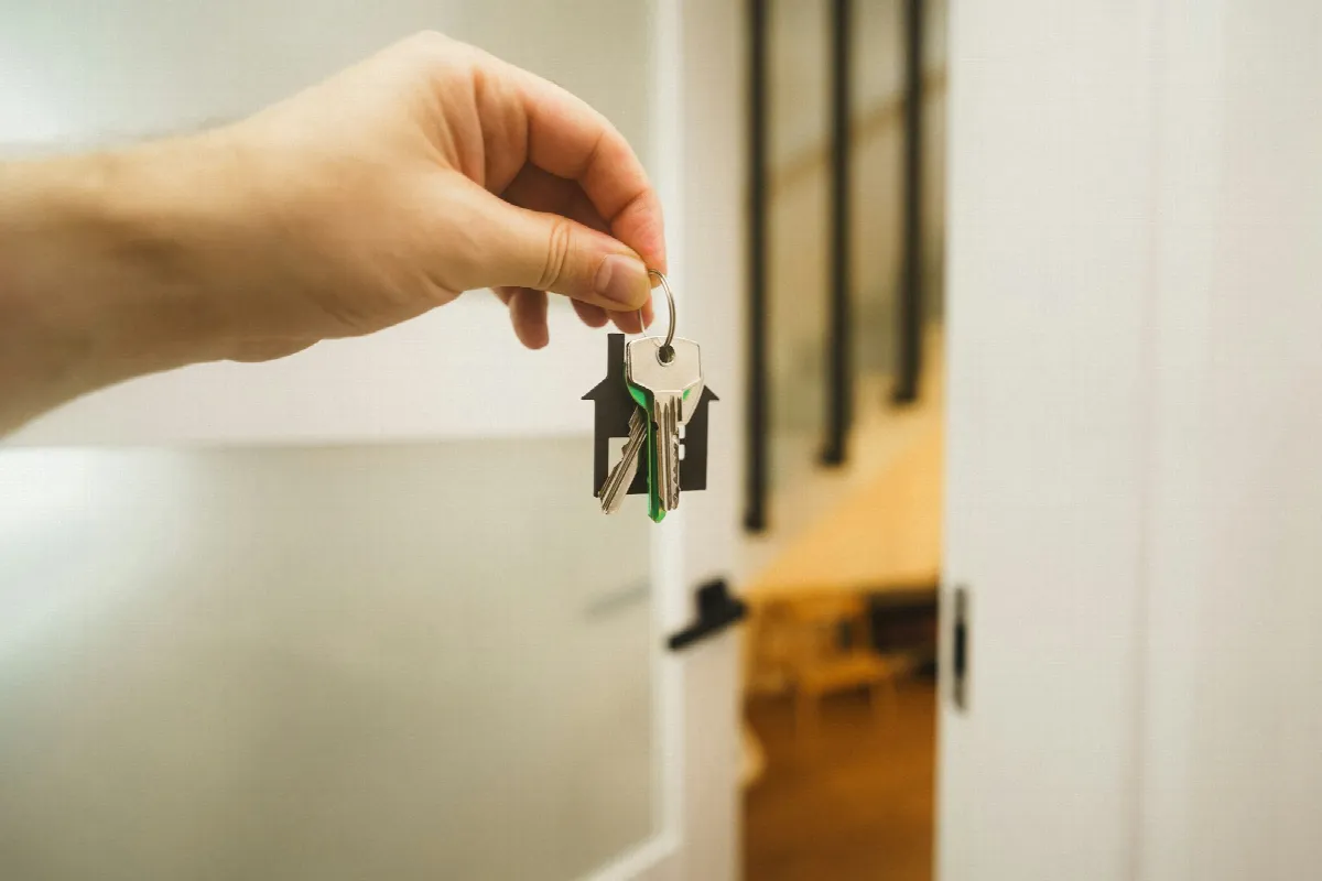 A hand holds up a set of house keys with a green key tag beside an open doorway