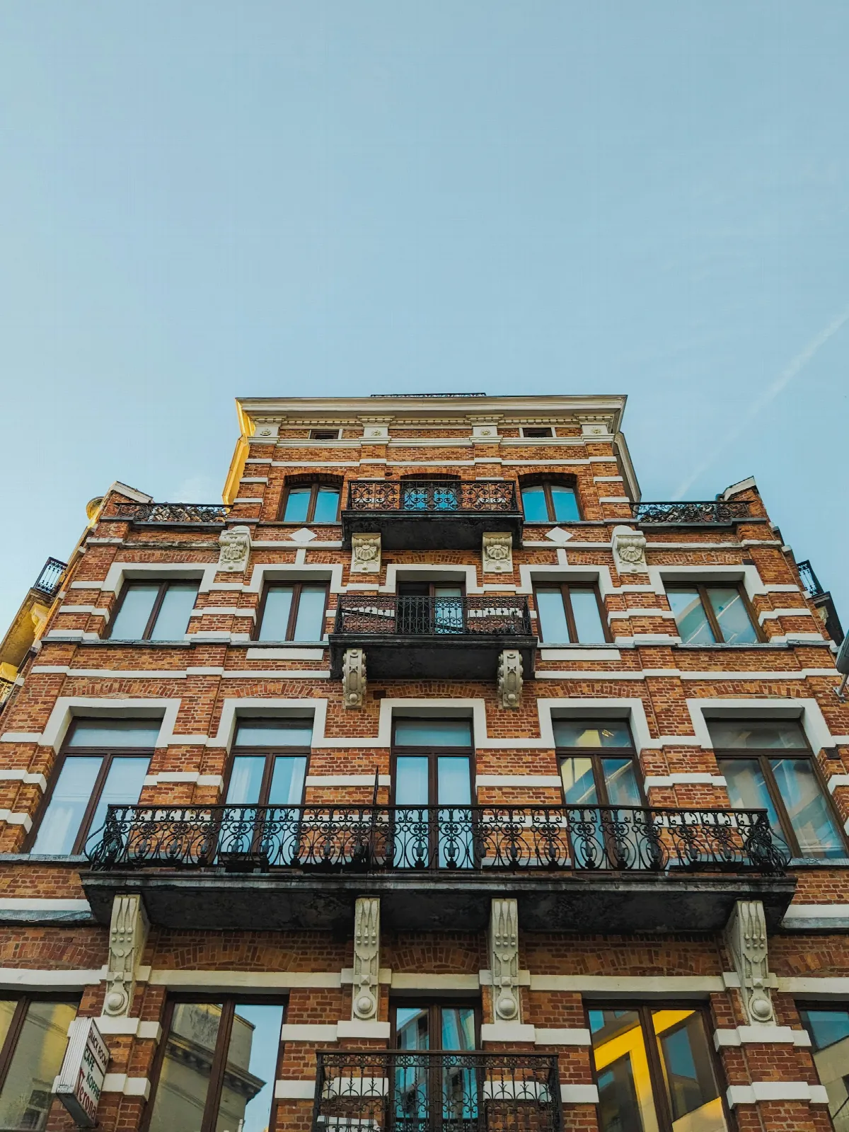 A tall brick apartment building with wrought-iron balconies against a clear blue sky
