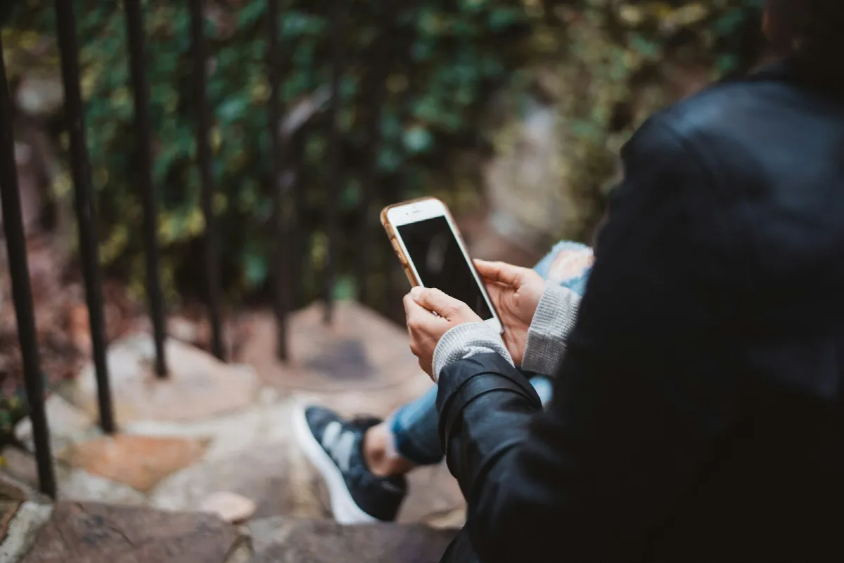A person sitting on outdoor stone steps reads a text on their smartphone, the way most landlords now pre-screen tenants before a showing