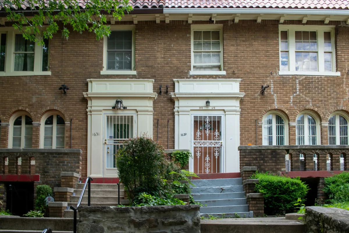 The brick front of a two-story row house with arched windows, white trim and steps leading up to the doors