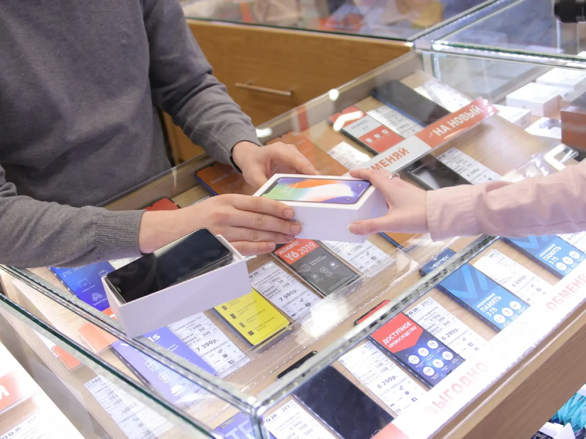 A store employee handing a boxed smartphone to a customer across a glass display counter