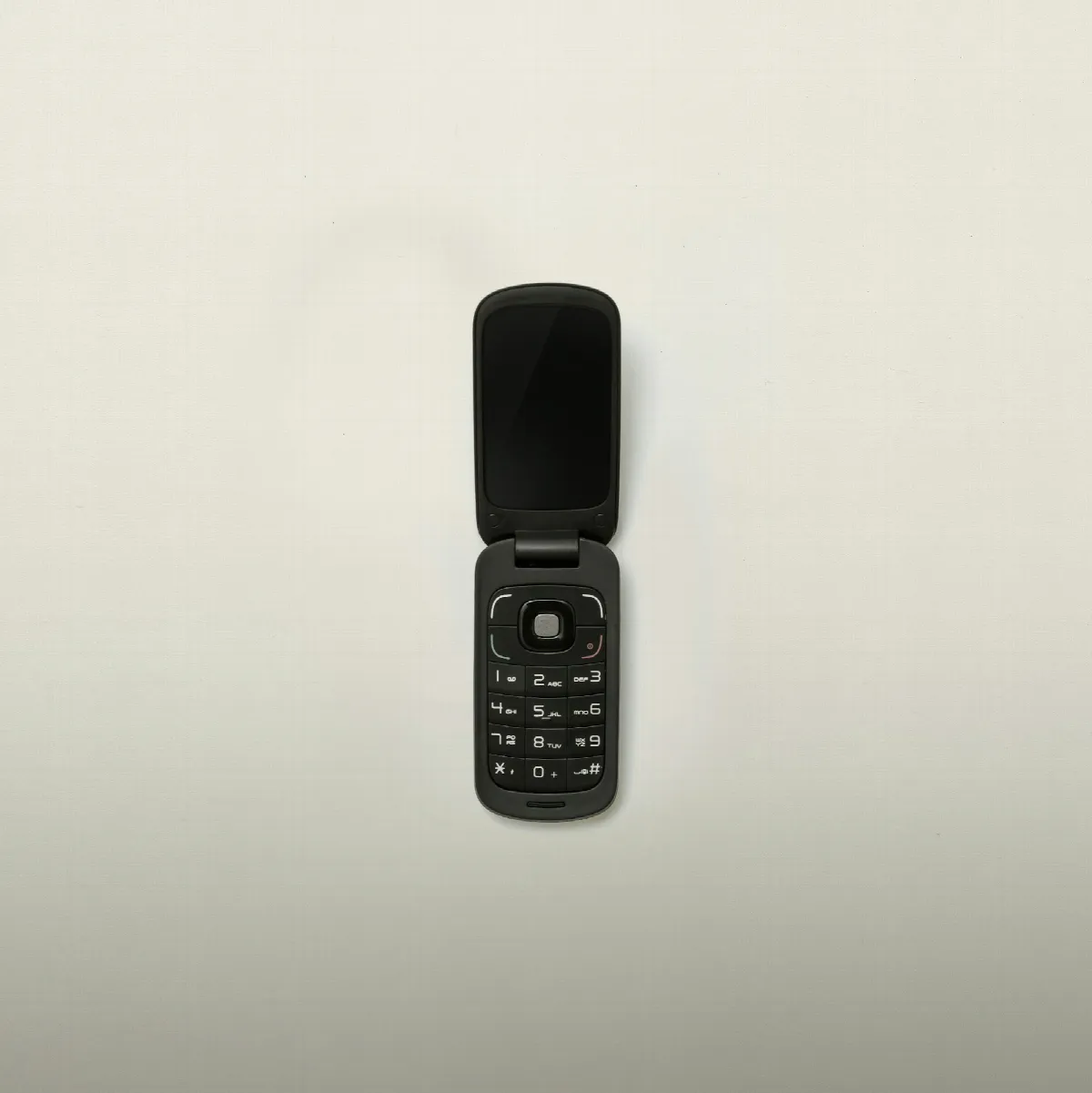 A black flip phone lying open on a pale gray surface