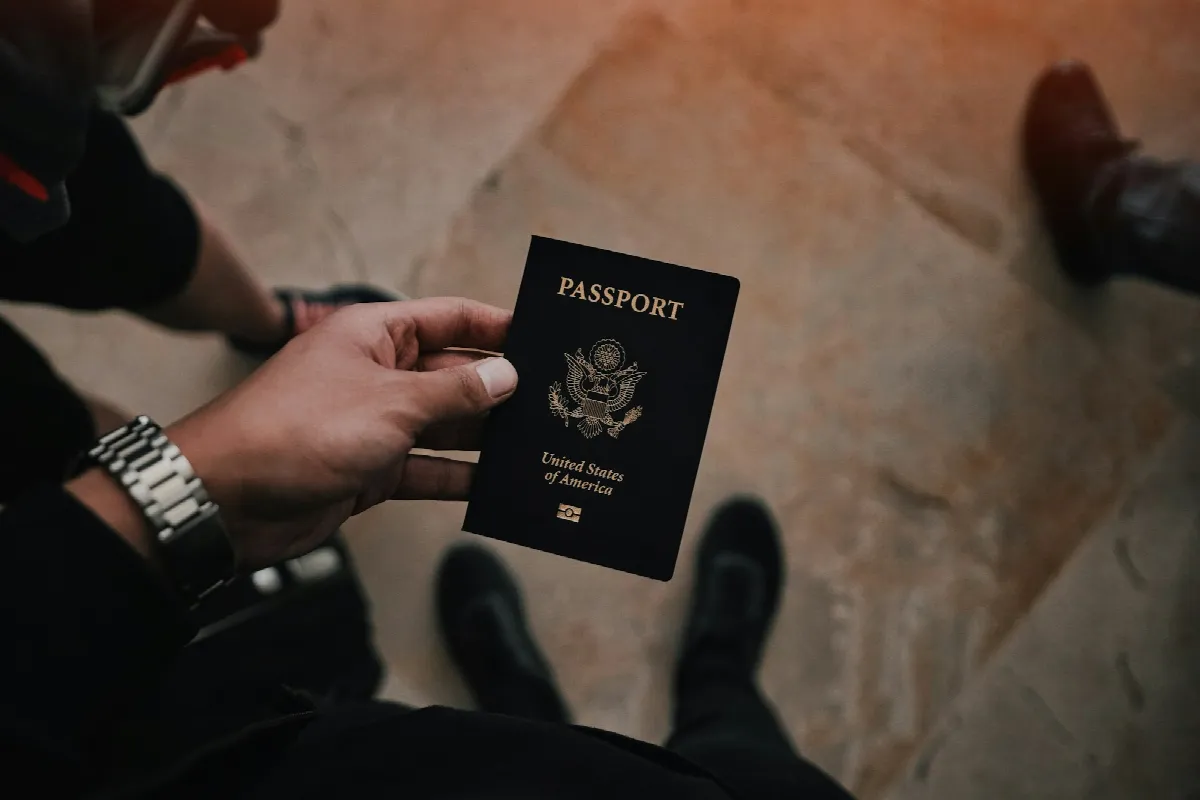 A person in a dark jacket holding a U.S. passport out toward the camera over a tiled floor