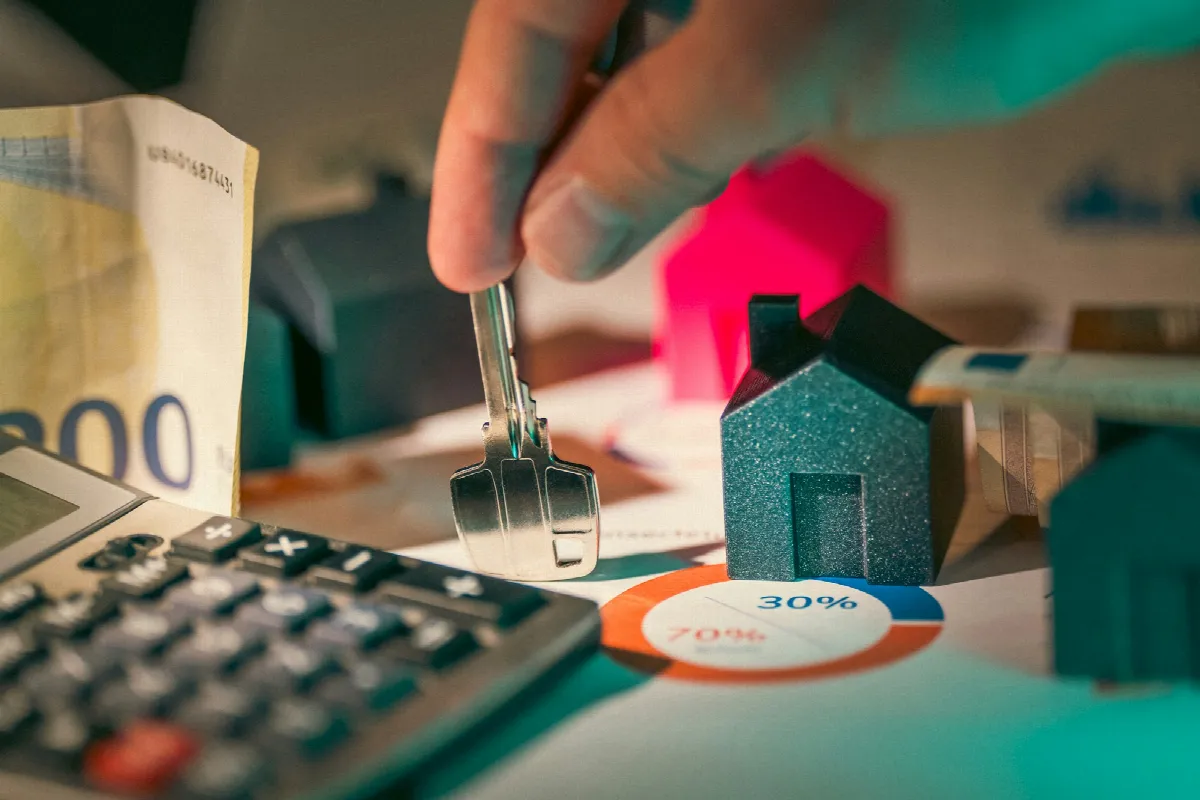 A hand holding a silver house key above small model homes, the hand-off that follows a tenant credit check