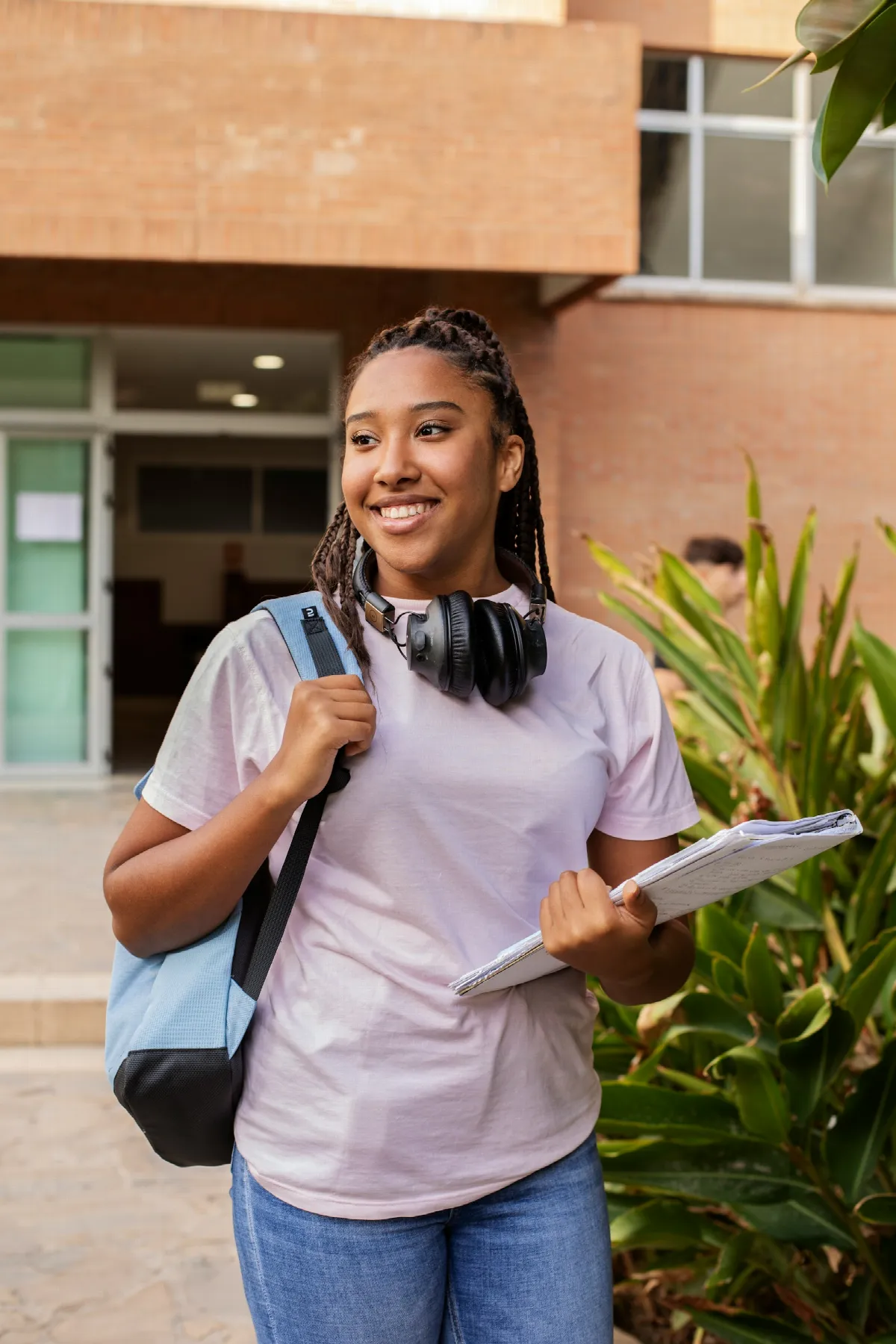 A smiling student carrying a backpack and books walks outside on campus