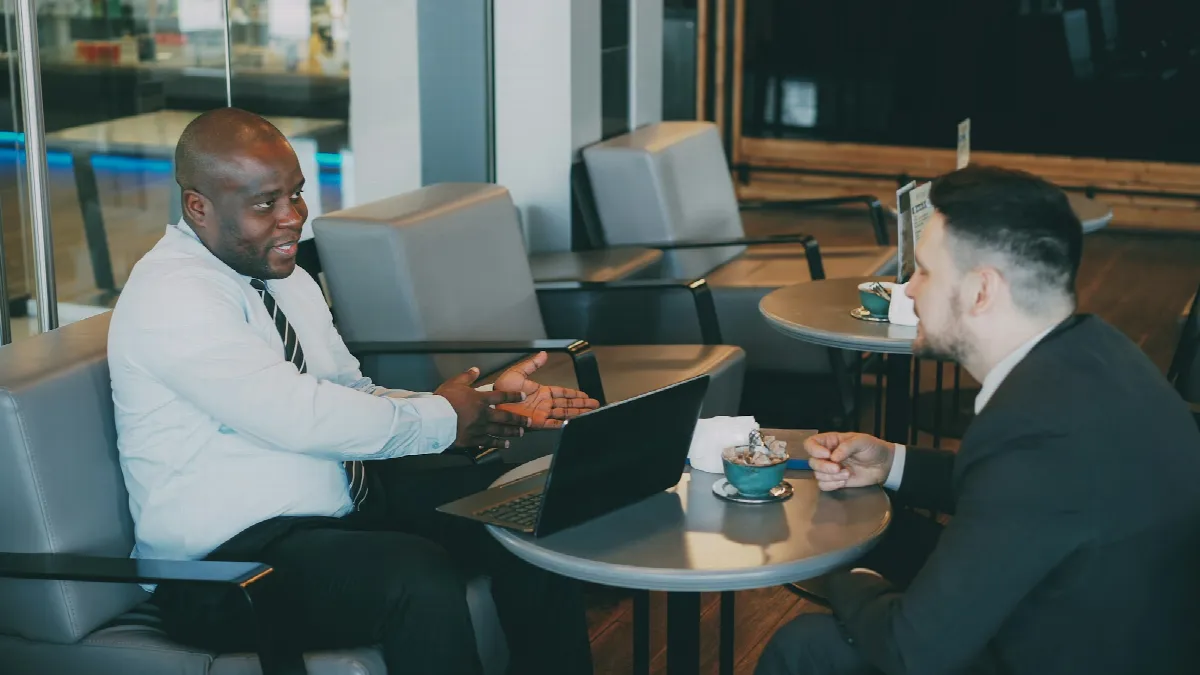 Two men in conversation at a cafe table with coffee cups between them