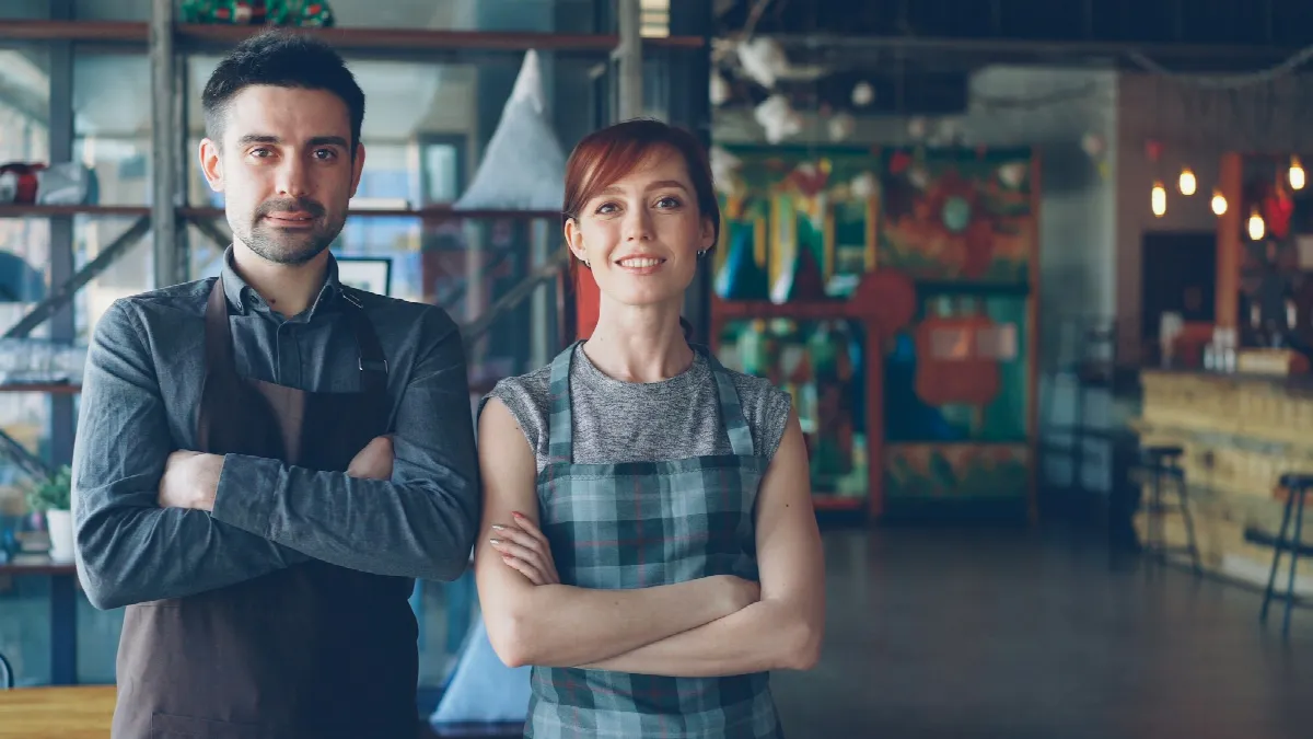 Two restaurant owners standing side by side with arms crossed in their dining room