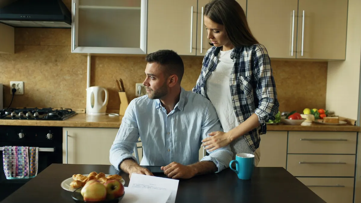 A man at a kitchen table checks his phone and paperwork while his partner looks on, working out what is a good credit score for their loan
