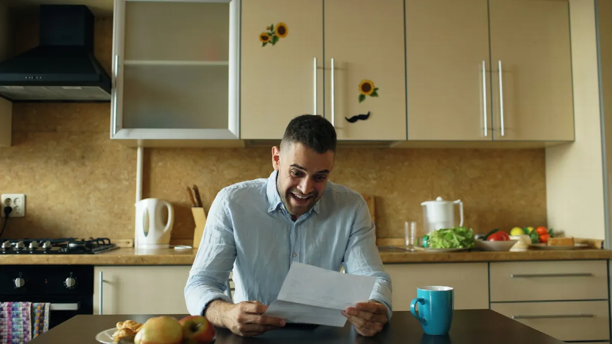 A man sitting at a kitchen table reading a letter