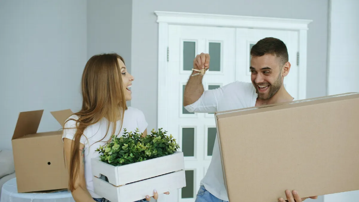 A young couple laughing in a new apartment, holding up a key between moving boxes