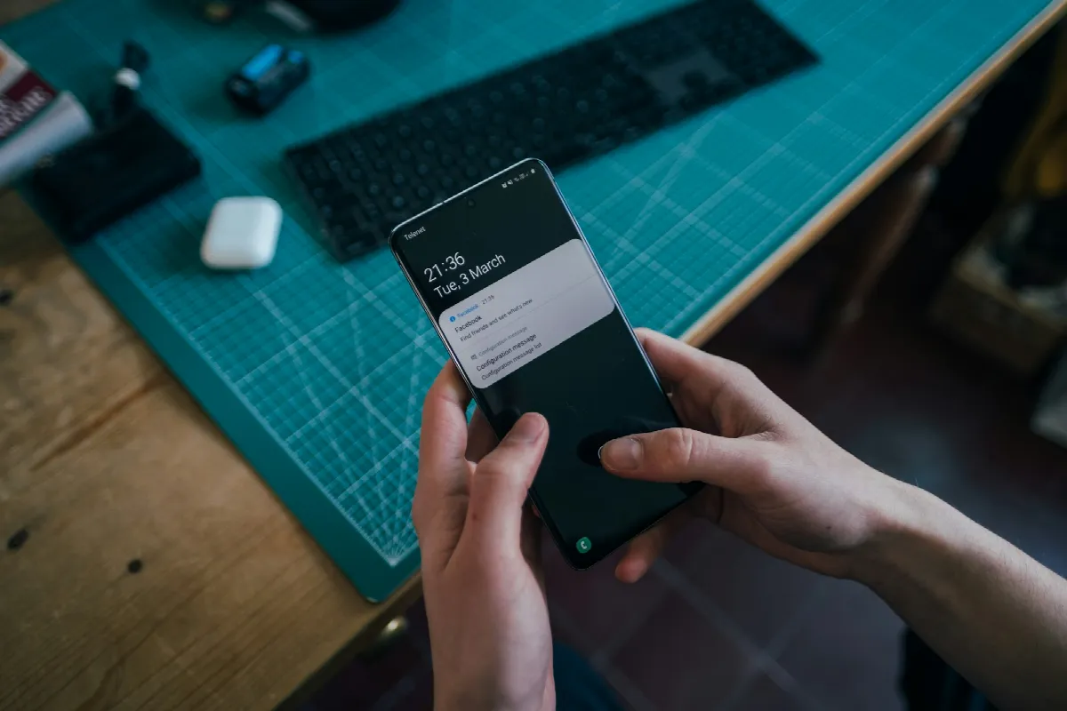 A young man at a desk holding a smartphone with notifications on its screen