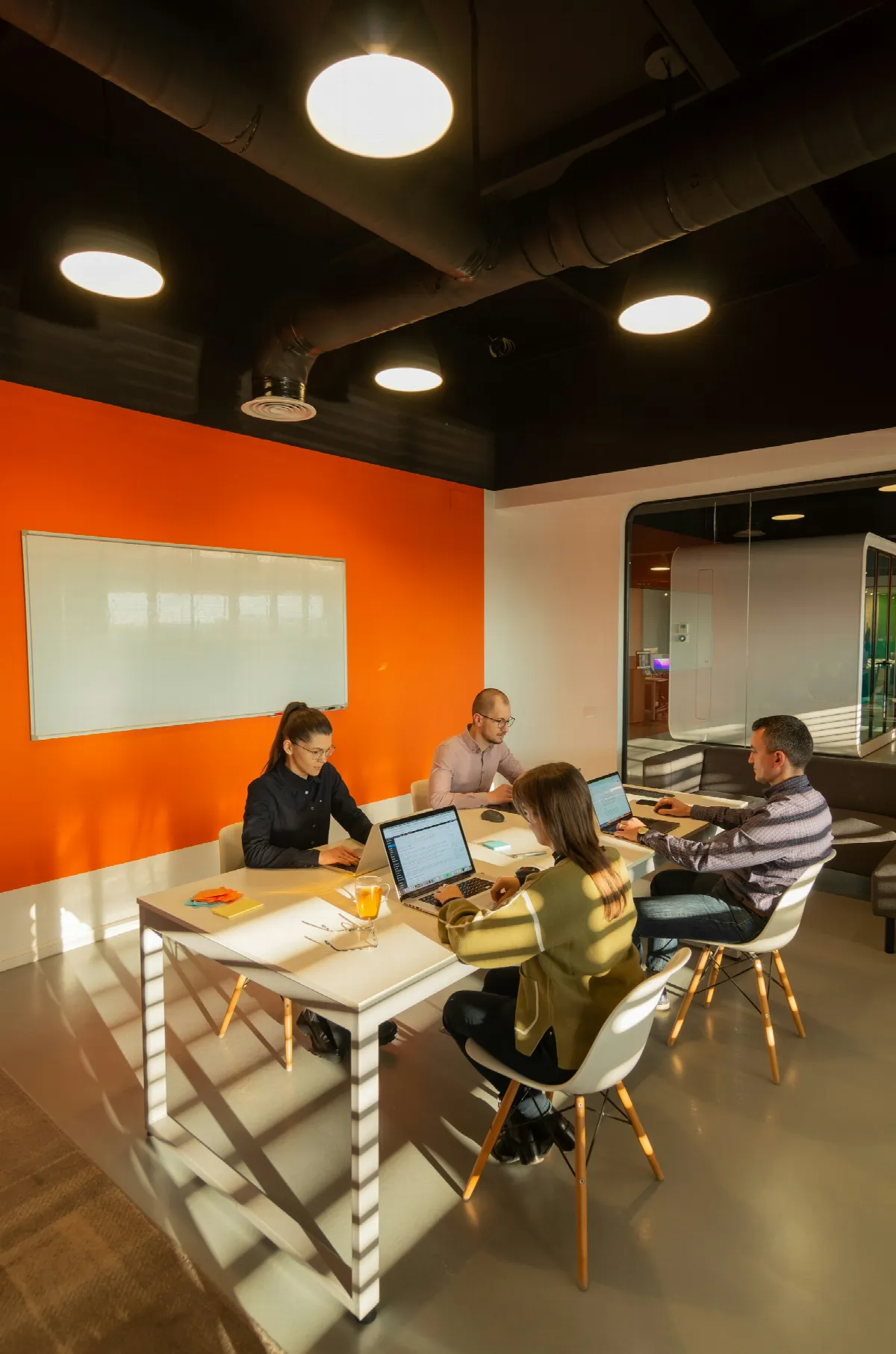 Four people working on laptops around a table in a modern meeting room