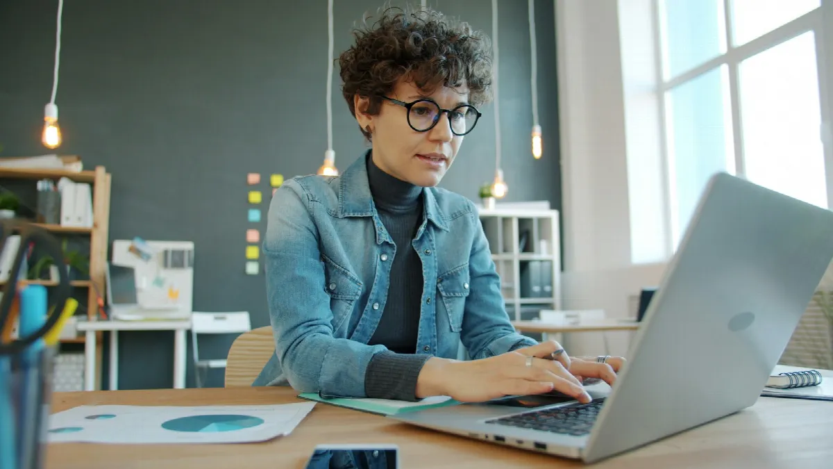 A woman typing on a laptop at a desk in a bright, modern office